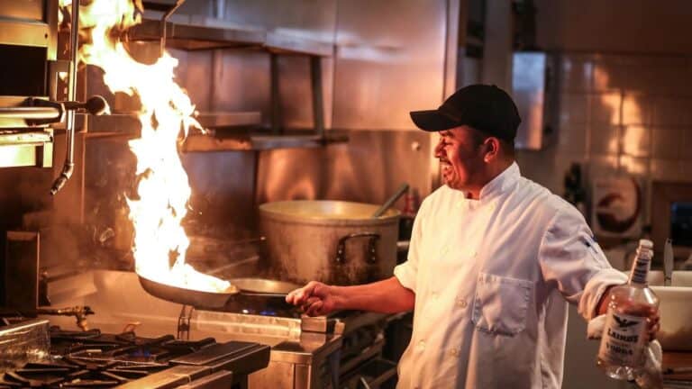 Chef flambéing with flames in a professional kitchen setting.