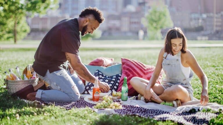 Young couple enjoying a boho-style picnic outdoors with food and drinks.