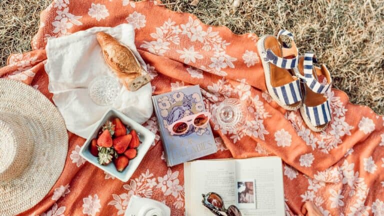 Charming boho picnic setup with strawberries, book, and sandals on a floral blanket.