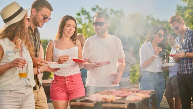 Outdoor barbecue with friends, grilling meat and sharing drinks on a sunny day.