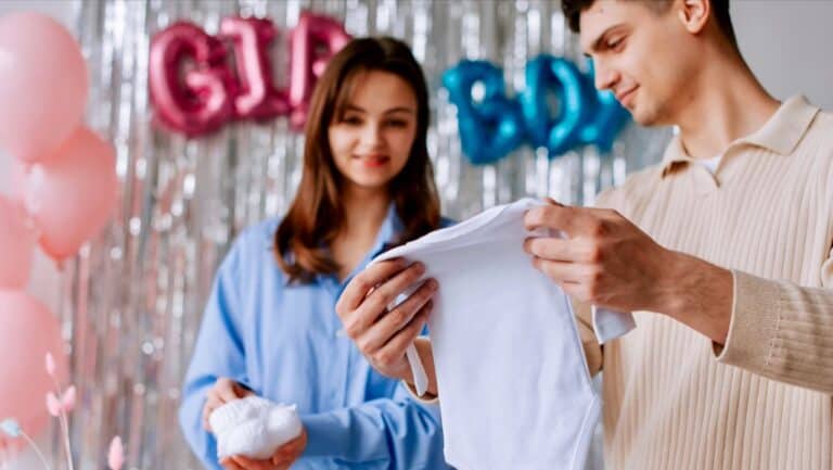 Man and woman opening a baby shower gift with pink and blue decorations.