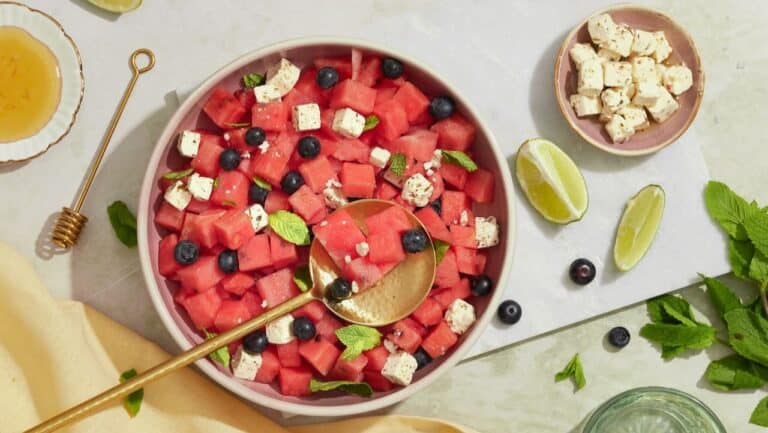 Fresh watermelon salad with feta cheese, blueberries, mint, and lime wedges for a refreshing summer.