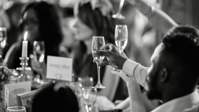 Celebration toast at wedding reception with guests raising glasses in black and white.