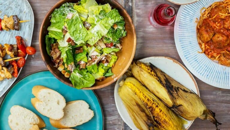 Fresh grilled corn and mixed greens salad served on rustic table for outdoor summer dinner gathering.