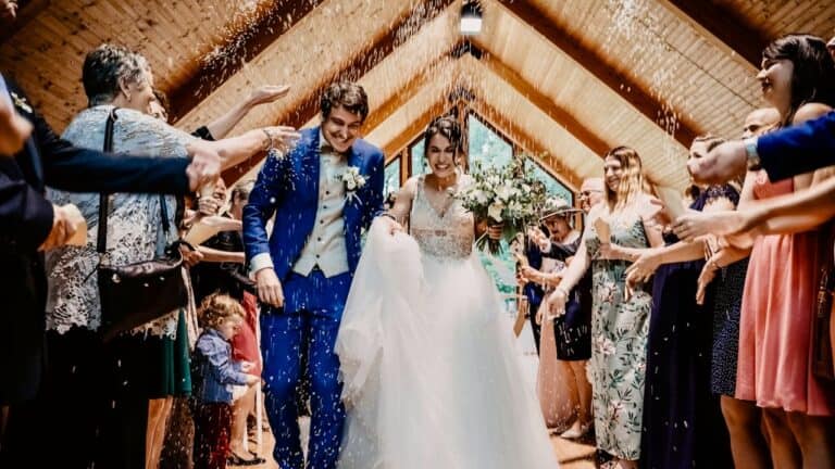 A wedding couple walking down the aisle with guests celebrating and throwing flower petals.