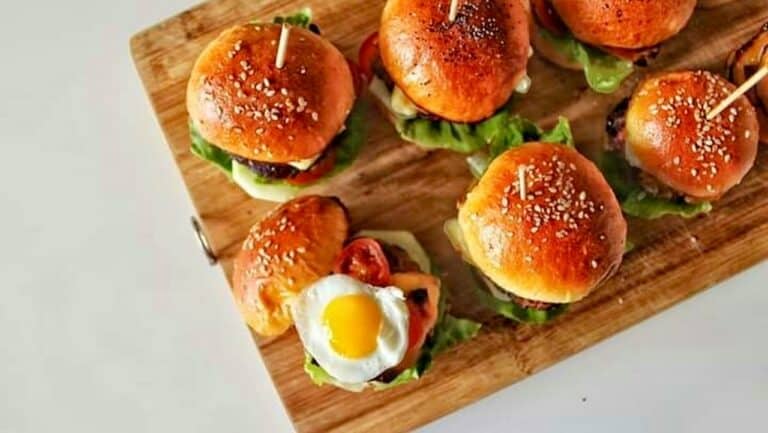 Mini sliders with lettuce, tomato, and a fried egg on a wooden board.