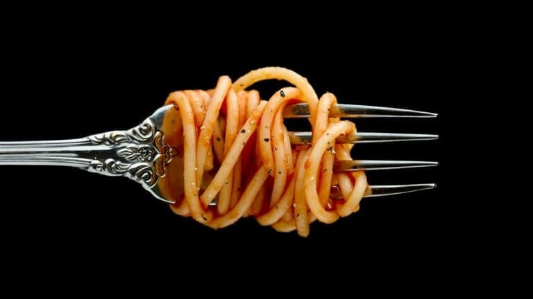 Spaghetti pasta twirled on a decorative fork against a black background.
