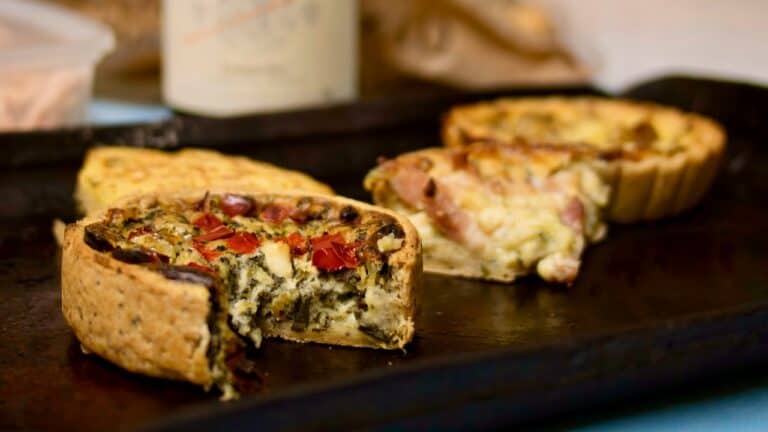 A delicious savory vegetable and cheese quiche with a flaky crust on a dark serving board.