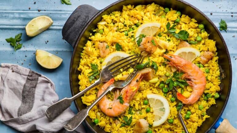 Bright yellow shrimp and lemon rice dish in a black skillet with fresh herbs and lemon wedges.