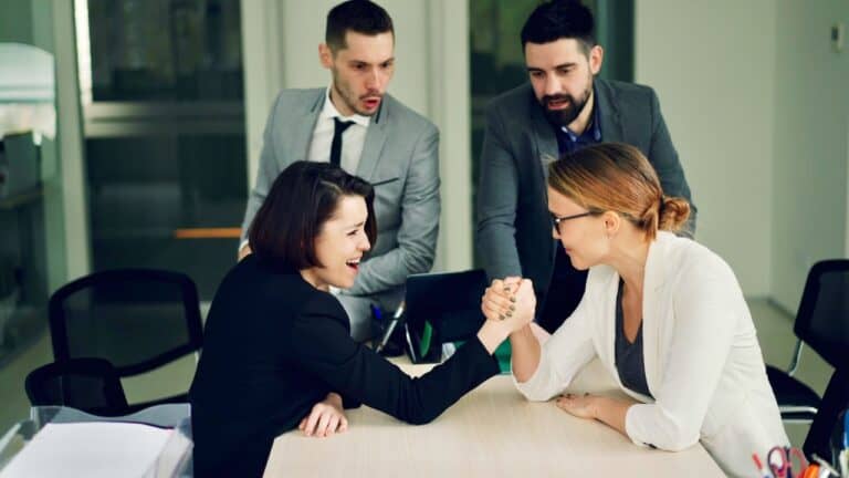 Engaged women arm wrestling in a professional business meeting setting.