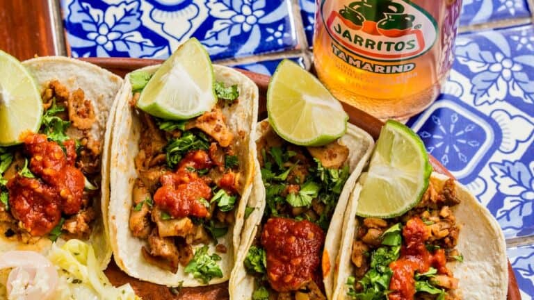Fresh Mexican tacos with seasoned meat, cilantro, and lime wedges on a vibrant blue and white patter.