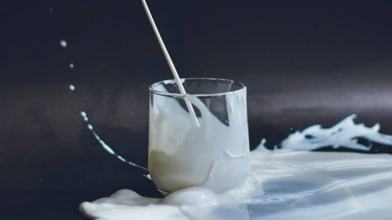 Creamy white beverage with a straw in a clear glass, splashing on a dark surface.