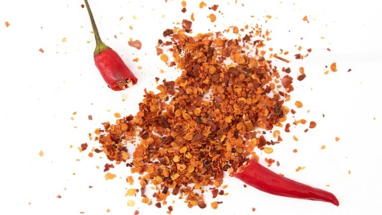 Smoked red chili flakes on white background with two whole chili peppers.