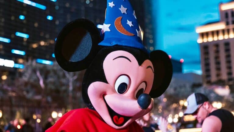 Cute Mickey Mouse wearing a wizard hat at night in an urban cityscape.