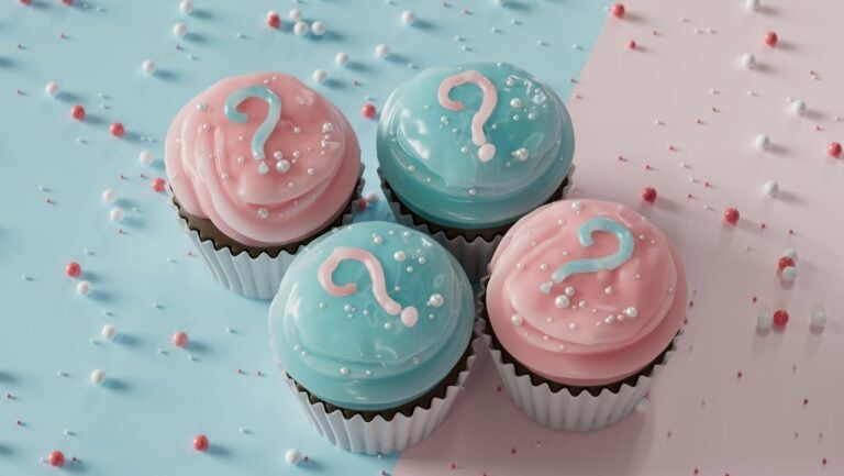 Pink and blue cupcakes with question mark decorations on pastel background.