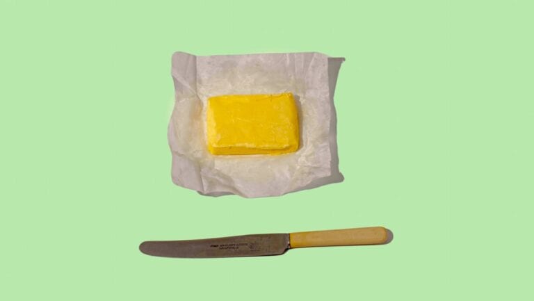 A delicious piece of yellow cheese on parchment paper with a cheese knife below.