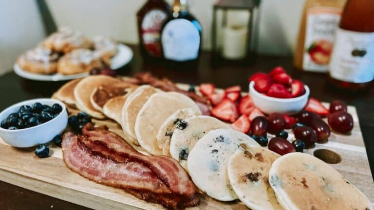 Delicious breakfast spread with blueberry pancakes, crispy bacon, fresh strawberries, and assorted t.