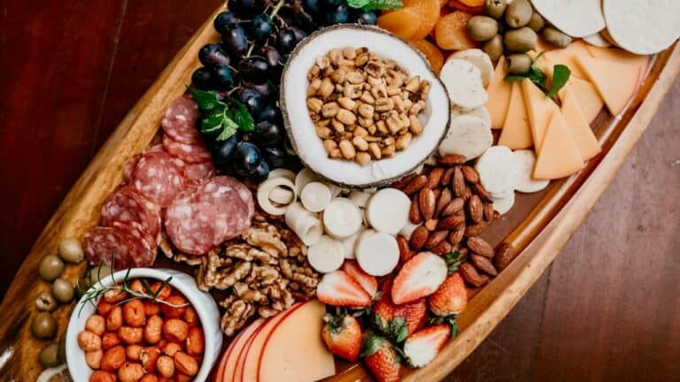 A variety of cheeses, nuts, fruits, and cured meats on a wooden serving board.