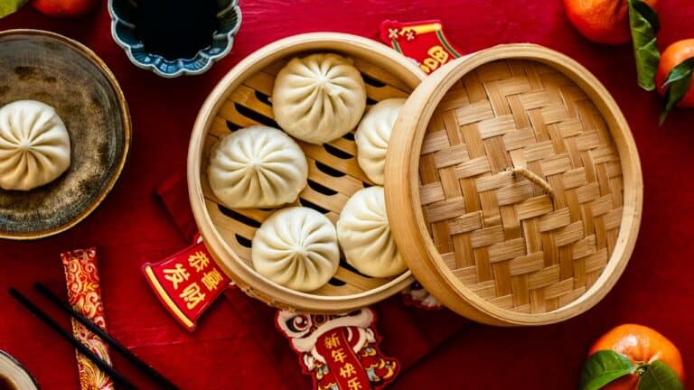 Steamed Chinese soup dumplings in bamboo steamer on red background.