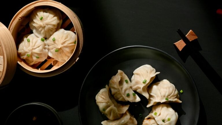 Steamed dumplings with green onion garnish on black plate, Asian cuisine, The Gourmet Host.
