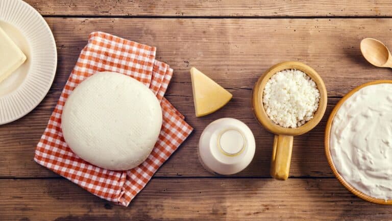 Fresh mozzarella cheese ball on a checkered cloth with dairy ingredients on a wooden table.