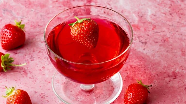 Strawberry Shirley Temple mocktail in a glass with fresh strawberries, pink background.