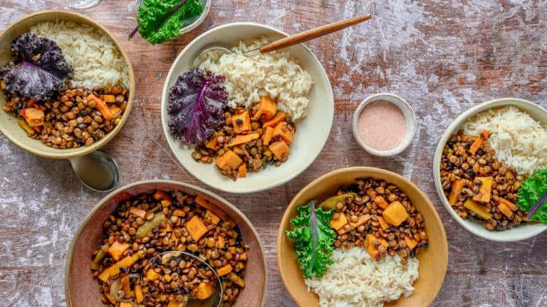 Hearty lentil and vegetable stew served with rice, garnished with fresh herbs on rustic wooden table.