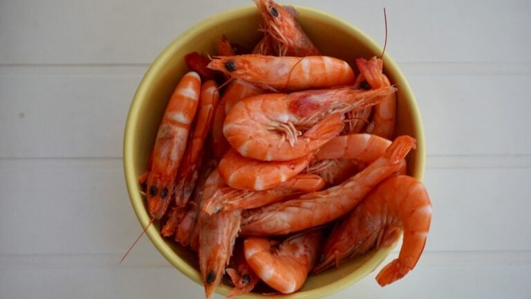Fresh cooked shrimp in a yellow bowl on a white wooden surface, seafood dish, gourmet cuisine, high-.