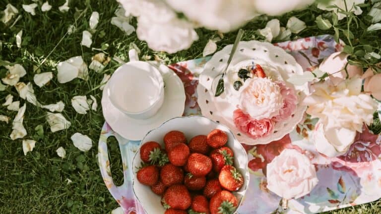 Fresh strawberries in a white bowl on a floral tray with white and pink roses, perfect for a gourmet.