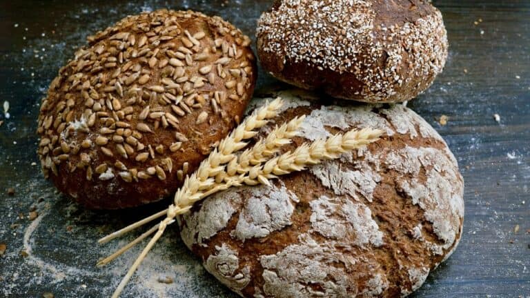 Freshly baked rustic bread with sunflower seeds, topped with powdered flour, on a wooden surface.