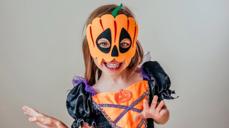 Cute child wearing a Halloween pumpkin mask and colorful costume, celebrating festive holiday fun.