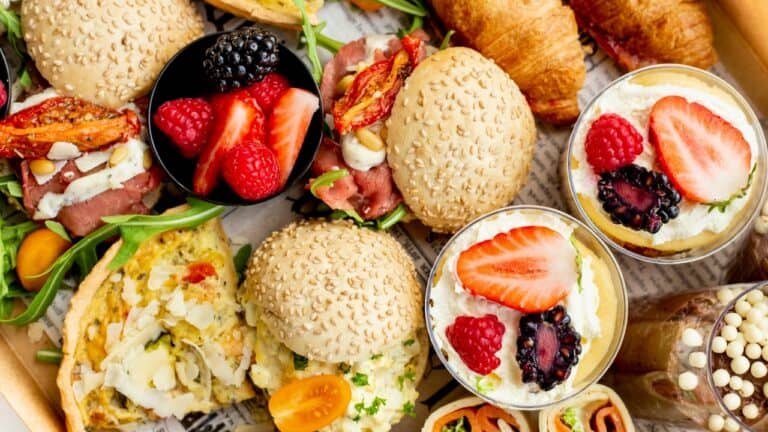Delicious assorted gourmet sandwiches, fresh berries, and creamy desserts on a platter.