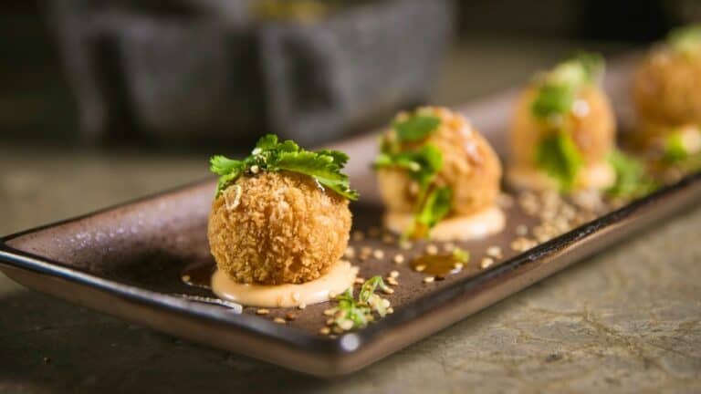 Fried appetizer balls garnished with herbs on a black rectangular plate.