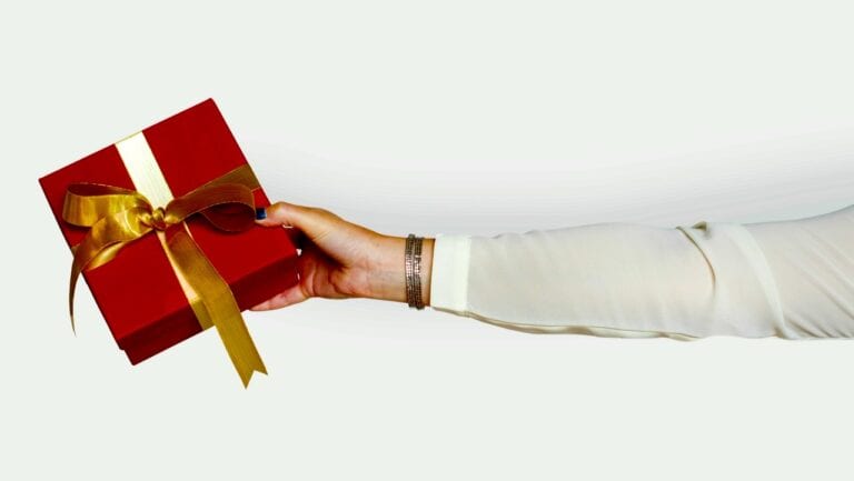 A gift box wrapped with a gold ribbon being held by a person in a white sleeve.