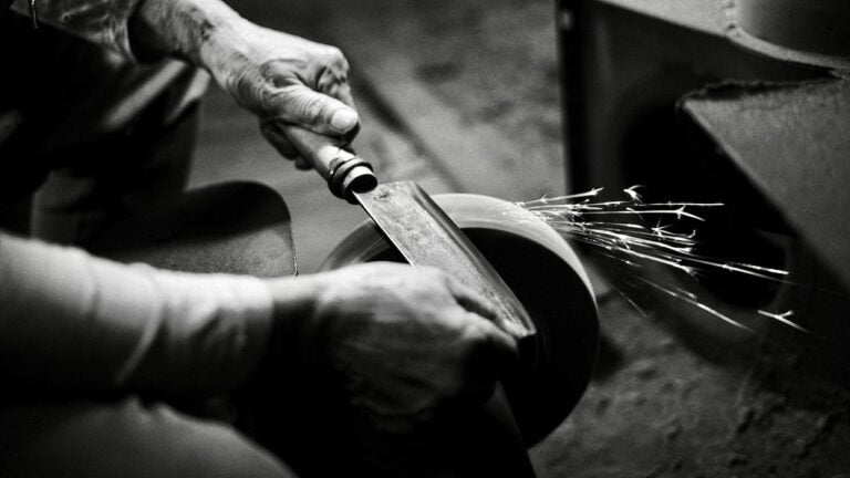 A sharp knife cutting through a ceramic bowl with sparks flying in a workshop setting.