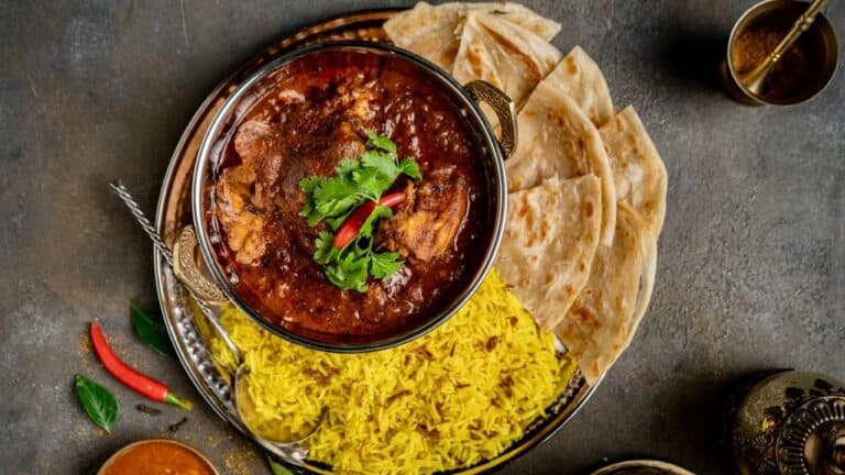 Spicy Indian curry with rice and naan bread on a dark surface.