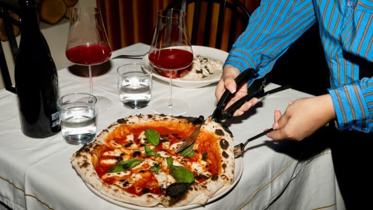 Authentic Margherita pizza being served at a dinner table with wine and water glasses.
