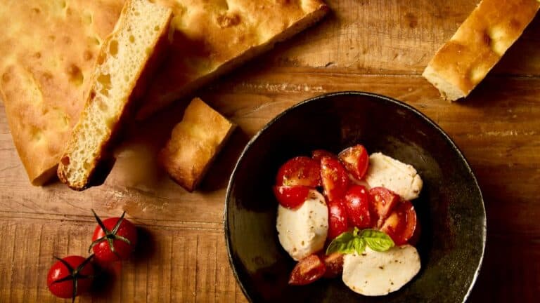 Fresh mozzarella, cherry tomatoes, and basil on a rustic wooden table, perfect for an Italian dinner.