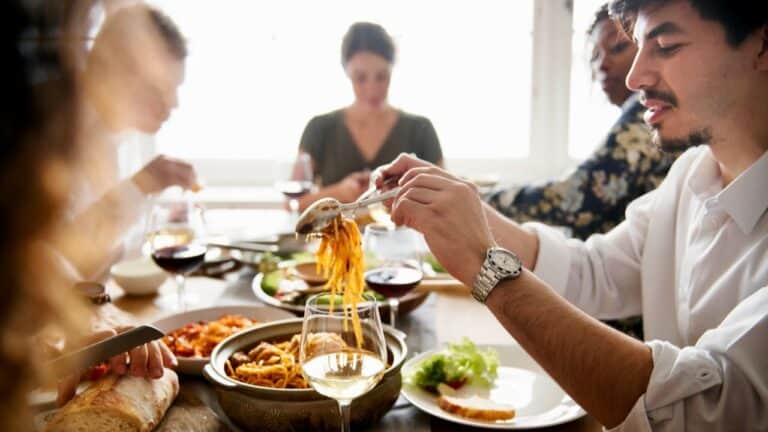 Group of friends enjoying Italian dinner with pasta, wine, and salads at a dinner party.