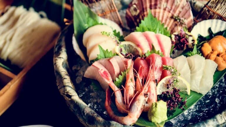Fresh seafood platter with shrimp, sashimi, and garnishes on a decorative plate.