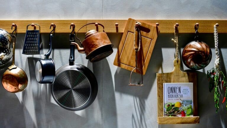 A colorful kitchen wall with hanging pots, pans, utensils, and a cookbook.