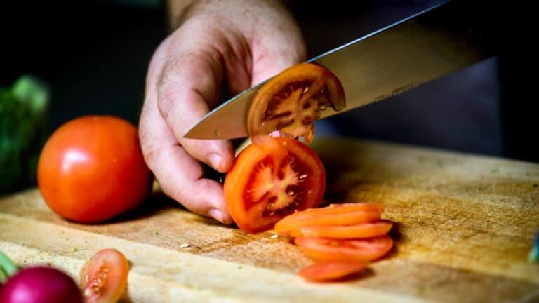 Fresh ripe tomatoes being sliced on a wooden cutting board for cooking or meal preparation.