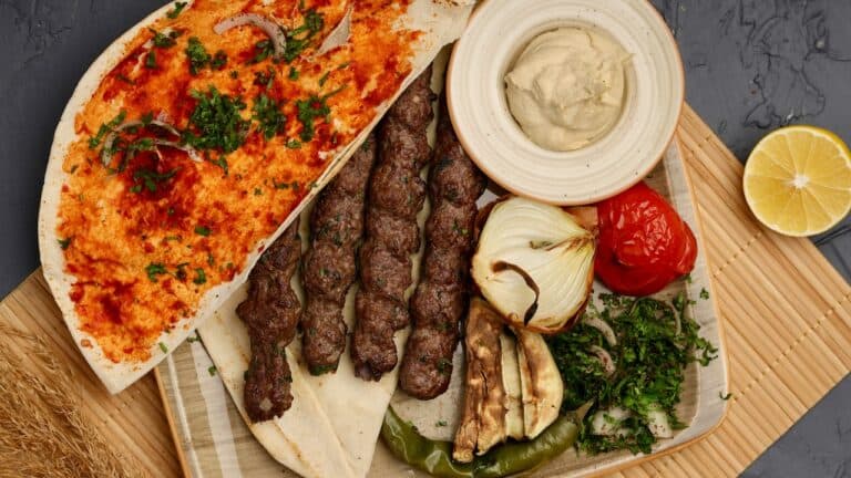 Grilled kebabs with vegetables, hummus, and lemon on a wooden platter.