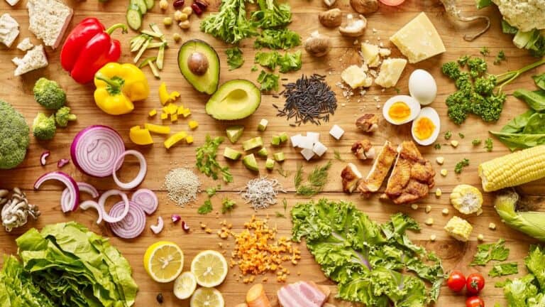 Fresh vegetables, cheese, eggs, and herbs arranged on a wooden surface for healthy cooking.