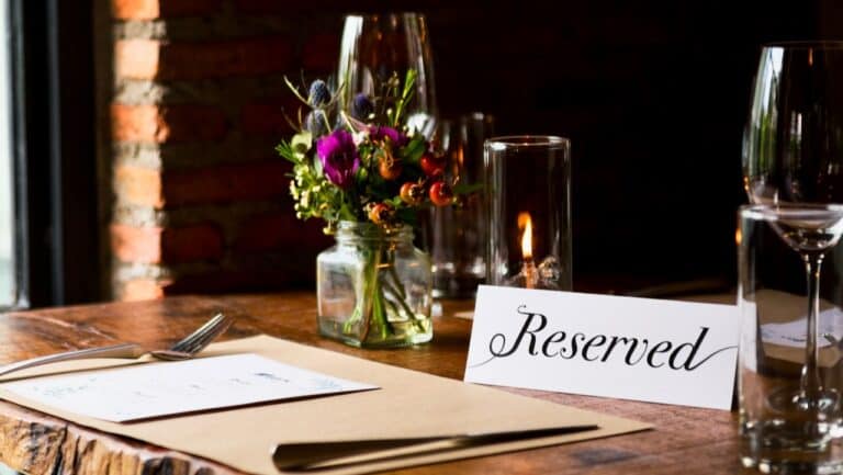 Elegant table setting with a "Reserved" sign, floral centerpiece, and glassware at The Gourmet Host.