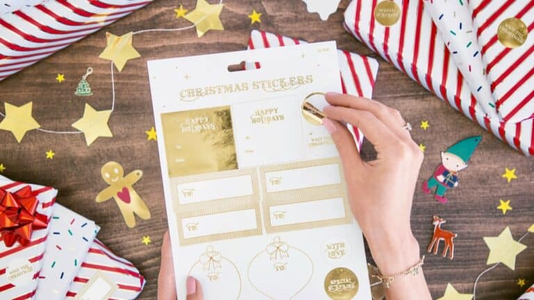Festive Christmas gift wrapping with holiday stickers, decorations, and a person's hand preparing pr.