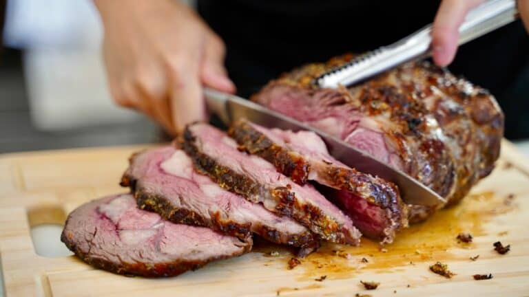 Juicy, perfectly cooked beef roast being sliced with a carving knife on a wooden cutting board.