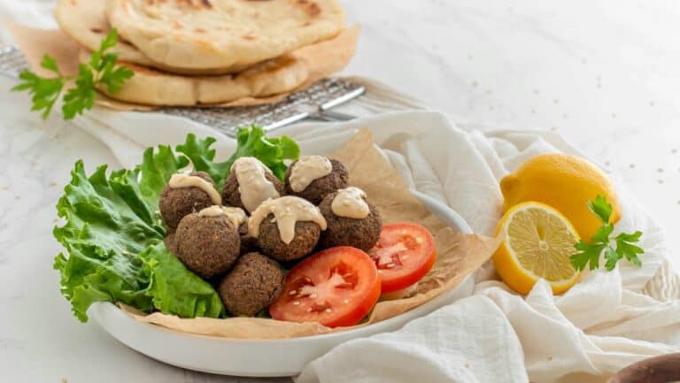 Fresh homemade falafel with lettuce and tomato slices on a rustic plate, served with lemon wedges fo.