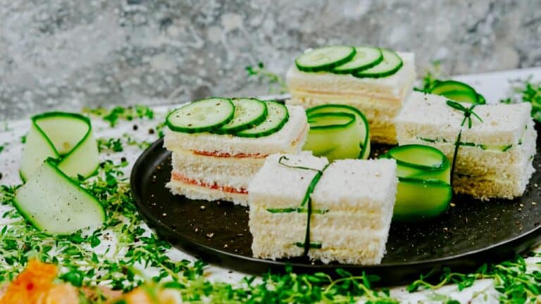 Fresh cucumber tea sandwiches on a black plate, garnished with cucumber slices and herbs.