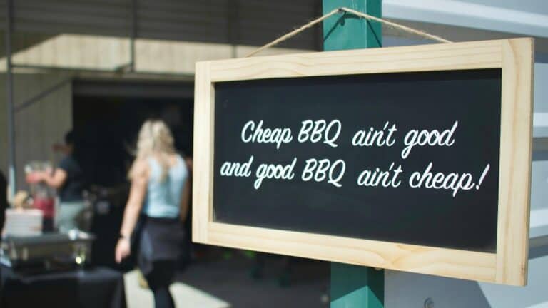 Chalkboard sign with humorous BBQ quote at outdoor event.